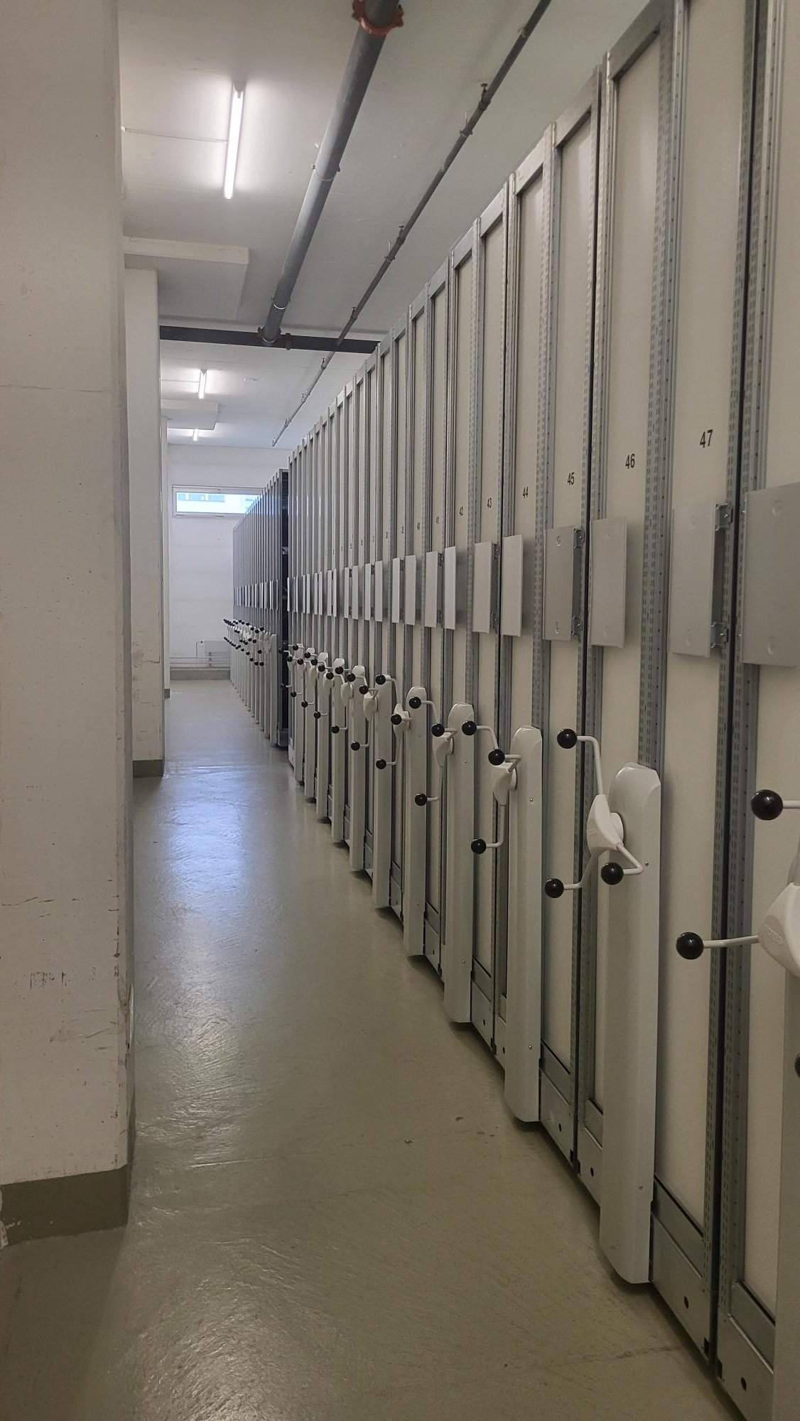 Storage units lined up, with numbers 40-47 on the doors, white walls, metallic beams, and a metal railing.