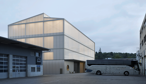 Modern building with glass walls, triangular roof, circular window, bus parked in front