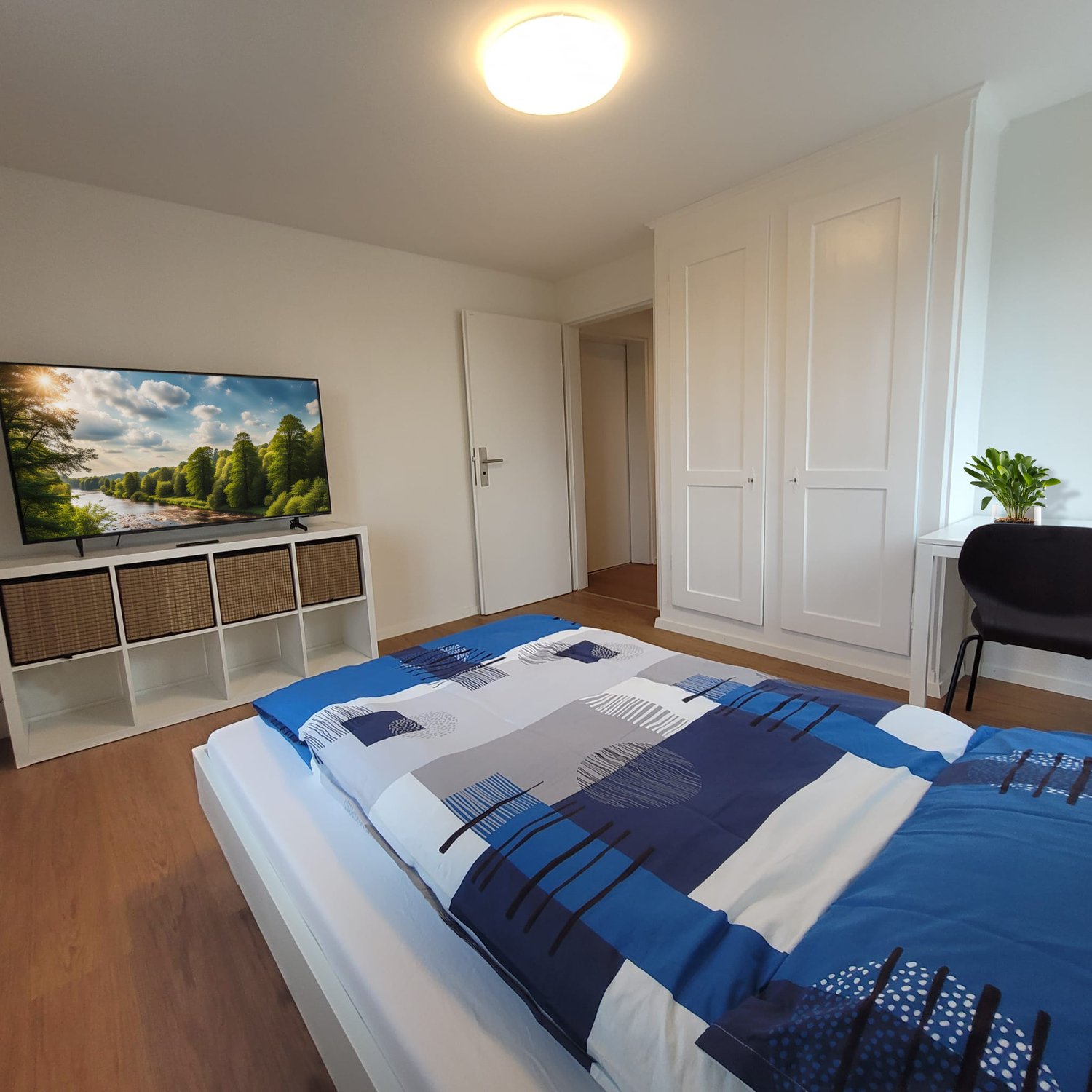 Large bed, white wall, TV stand, wardrobe, wooden floor, desk, chair
