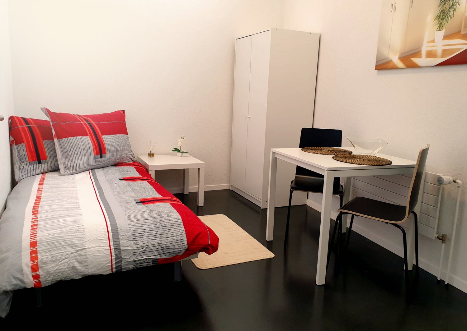 Single bed, pillows, nightstand, table, chairs, white wardrobe, wall painting