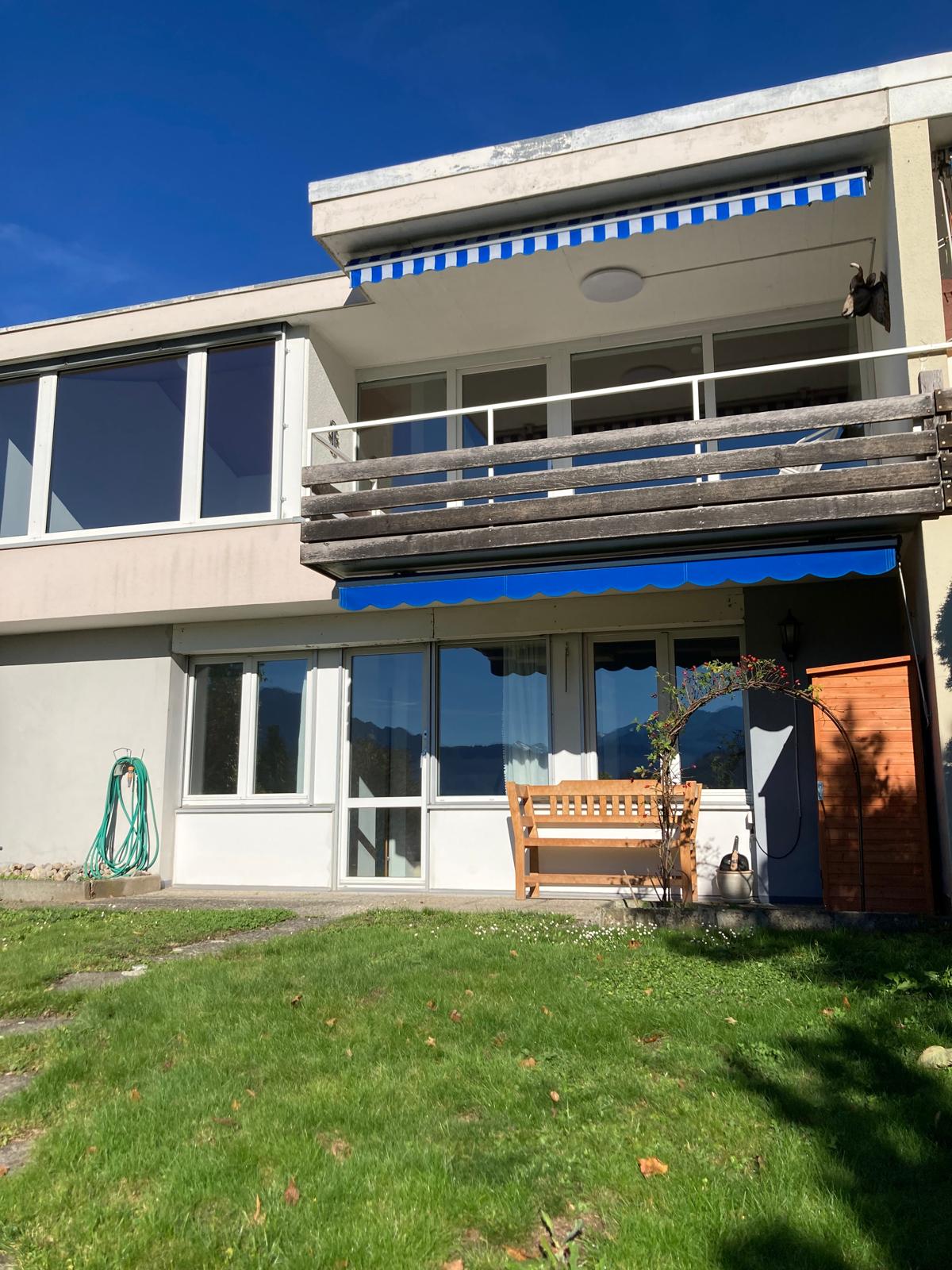 Detached house, two floors, beige walls, white windows, wooden balcony, white garage door, garden
