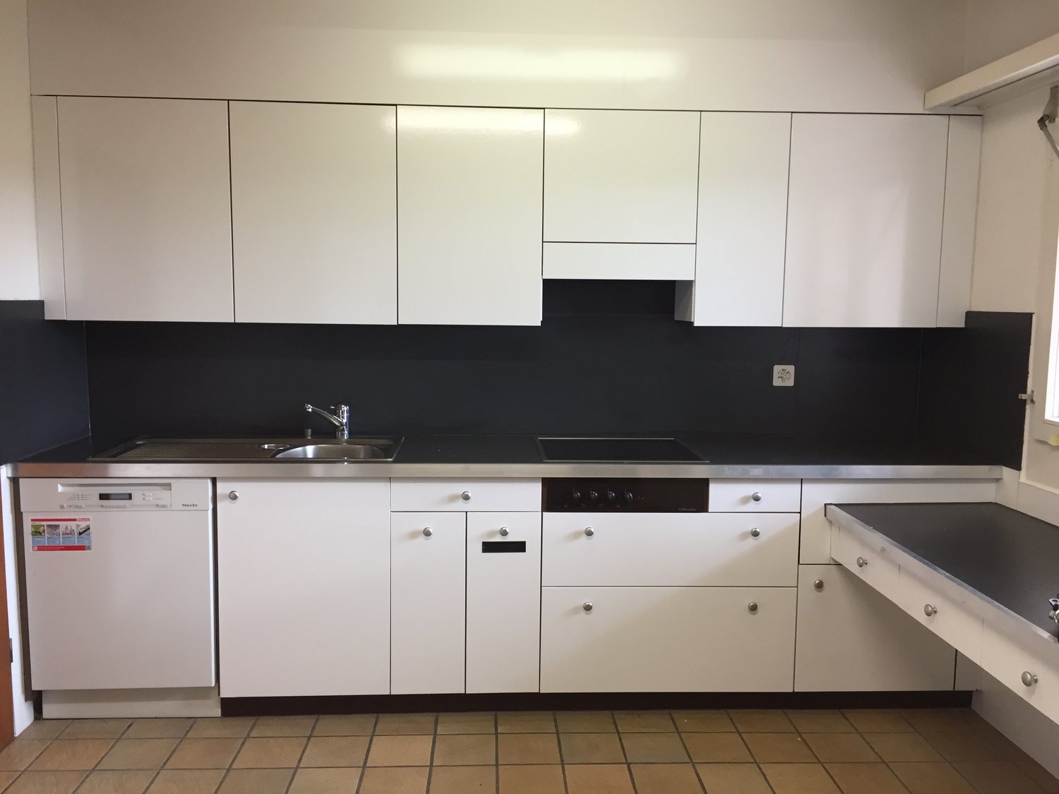 Modern white kitchen cabinets, black countertop, built-in dishwasher, stove, and sink