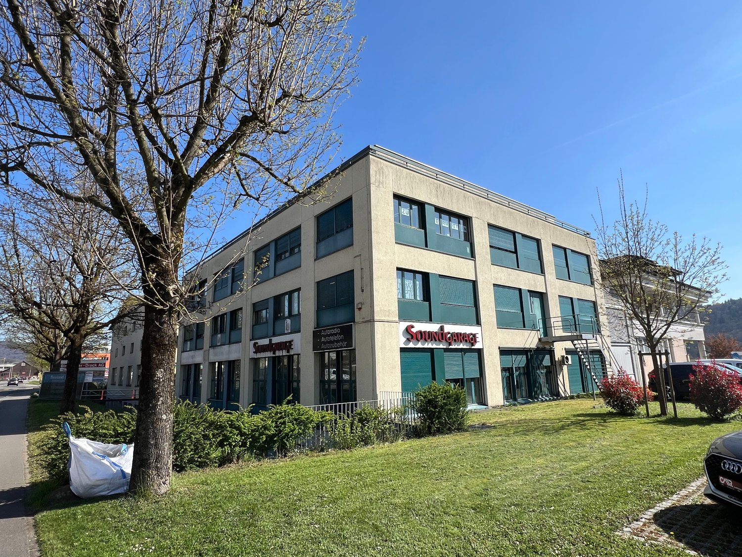 2-story commercial building with a Sound Garage sign, surrounded by trees and grass, with a parking area in front.