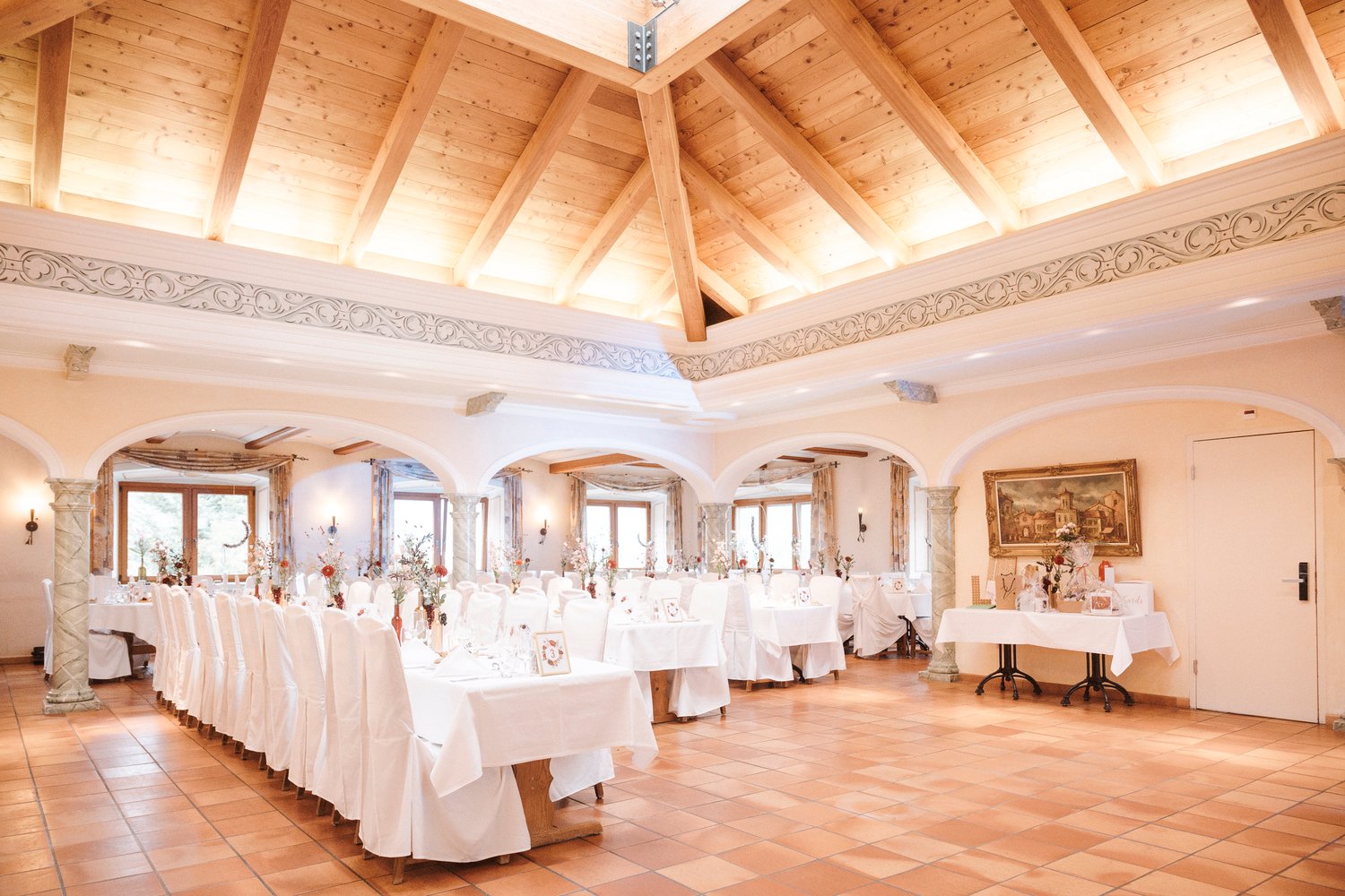 Large dining room with high wooden ceiling, ornate molding, arched windows, white tablecloths, and a fireplace