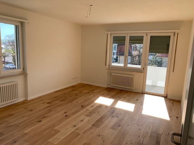 empty room, hardwood floor, two large windows, sliding door, balcony, white walls, white radiators