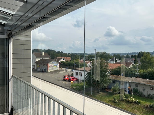 large glass window, balcony, parked cars, green grass, street