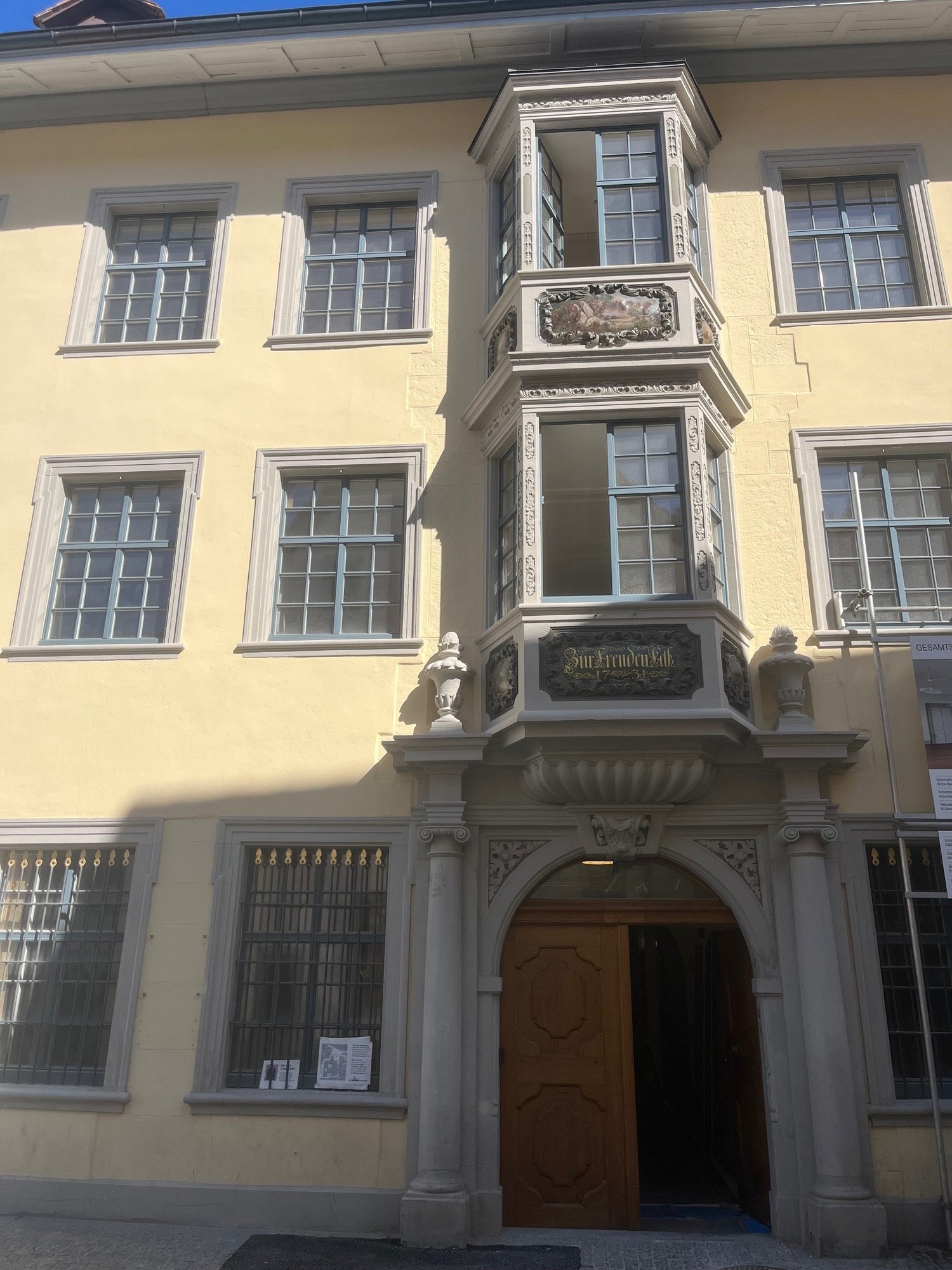yellow building, multiple windows, wooden door, balcony with intricate design, decorative elements