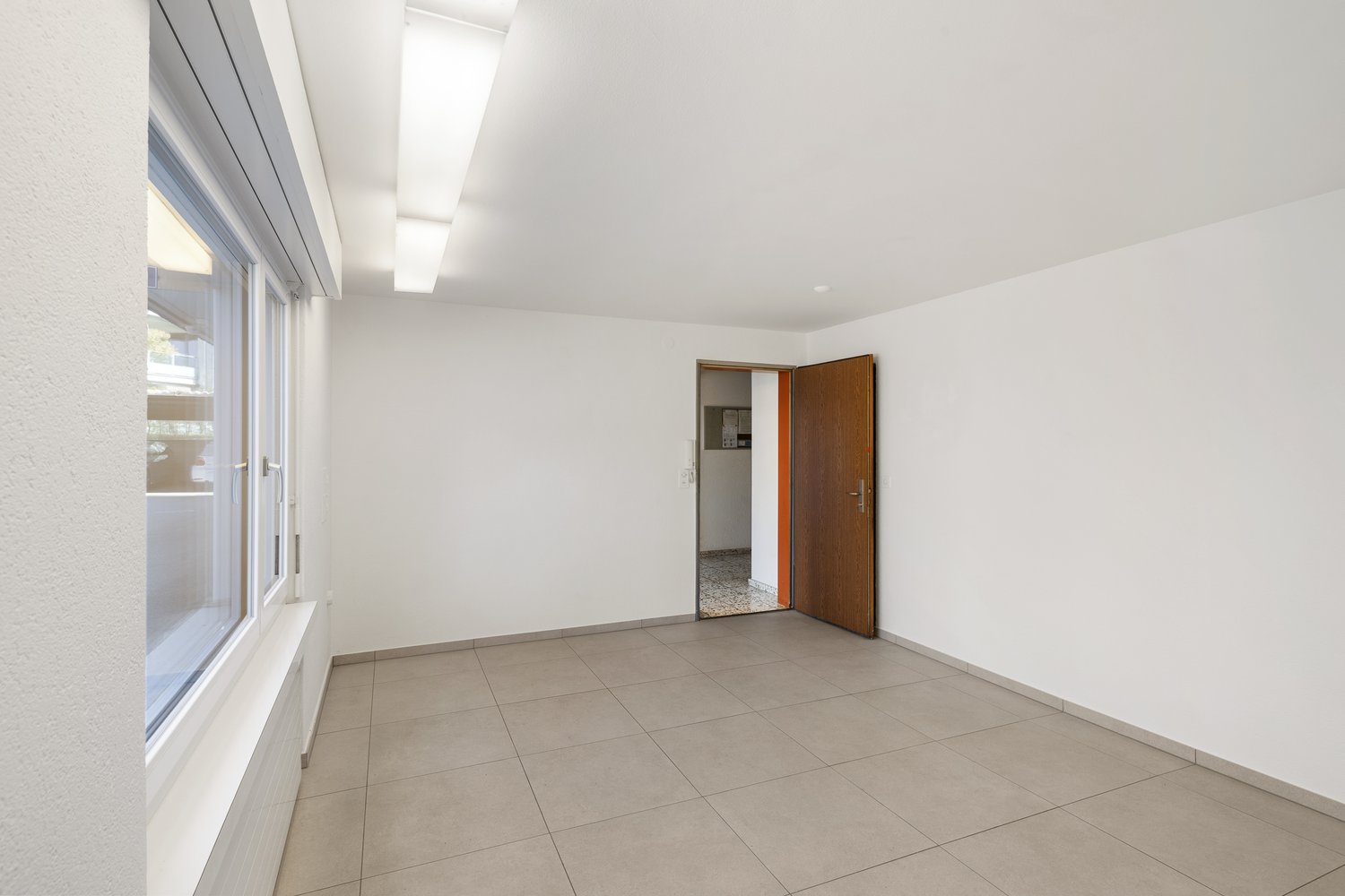 Empty room with white walls, tiled floor, large window, open door leading to another room