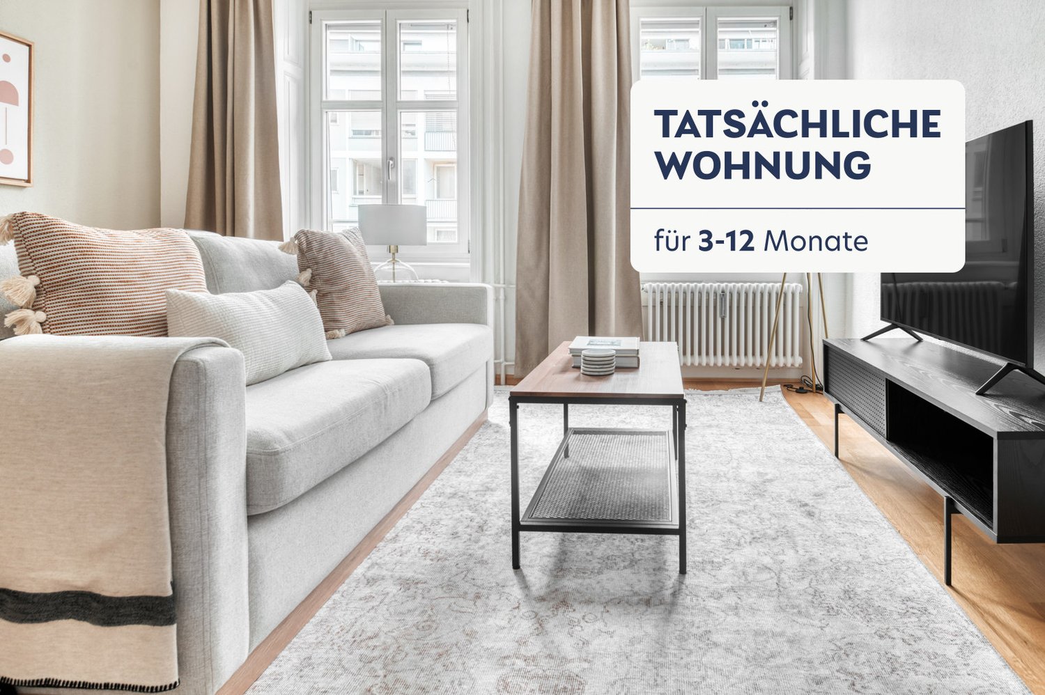 Spacious living room with large windows, light-colored sofa, coffee table, and TV stand. The room has a cozy and modern feel with neutral tones and textured accents.