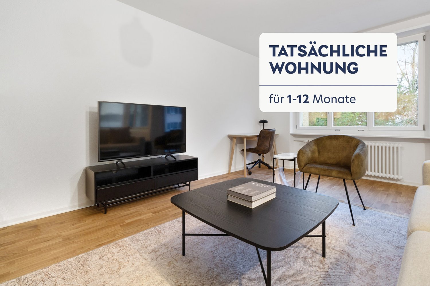 Spacious living room with hardwood floors, large windows, TV stand, coffee table, and a comfortable armchair. The room has a modern and minimalist design.