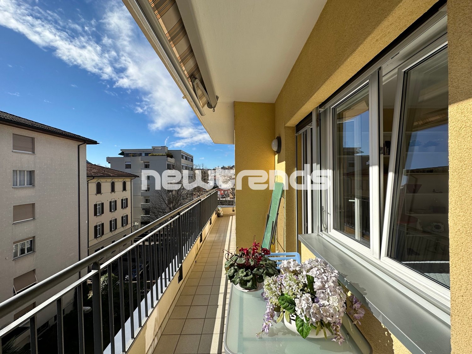 Balcony with railings, flowers, potted plants, and a view of the street.