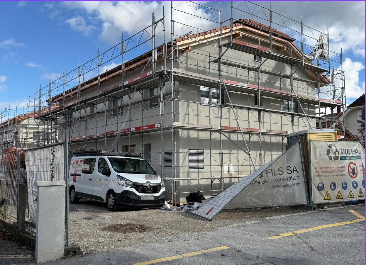 Under construction white painted 4-story house, with scaffolding, red tile roof, windows, and parked van