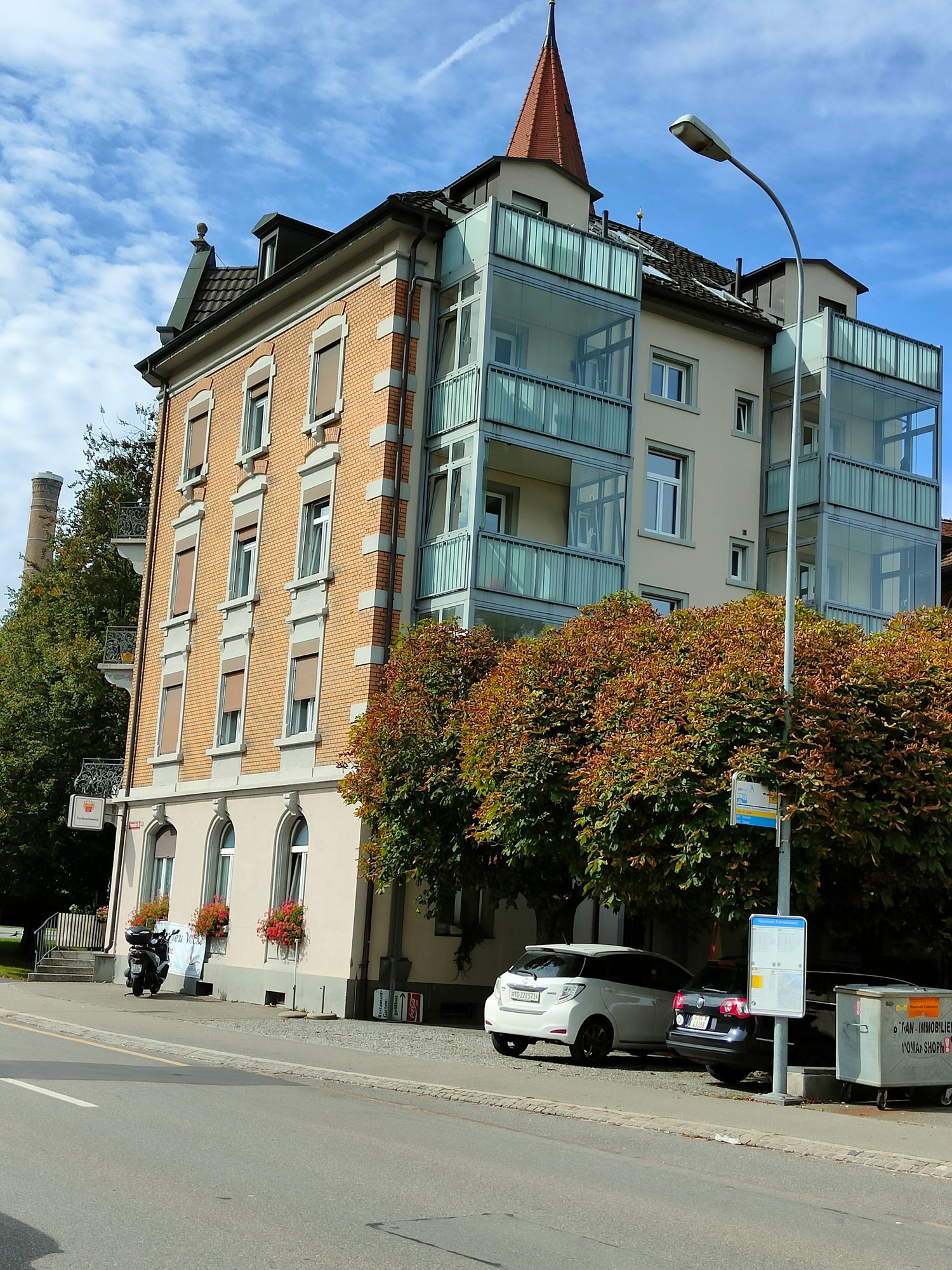 5 story building, brick and glass walls, balconies, two cars parked in front