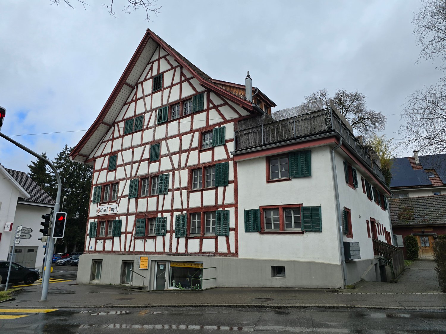 white and brown house, multiple windows, red and green shutters, brick chimney, balcony on top floor
