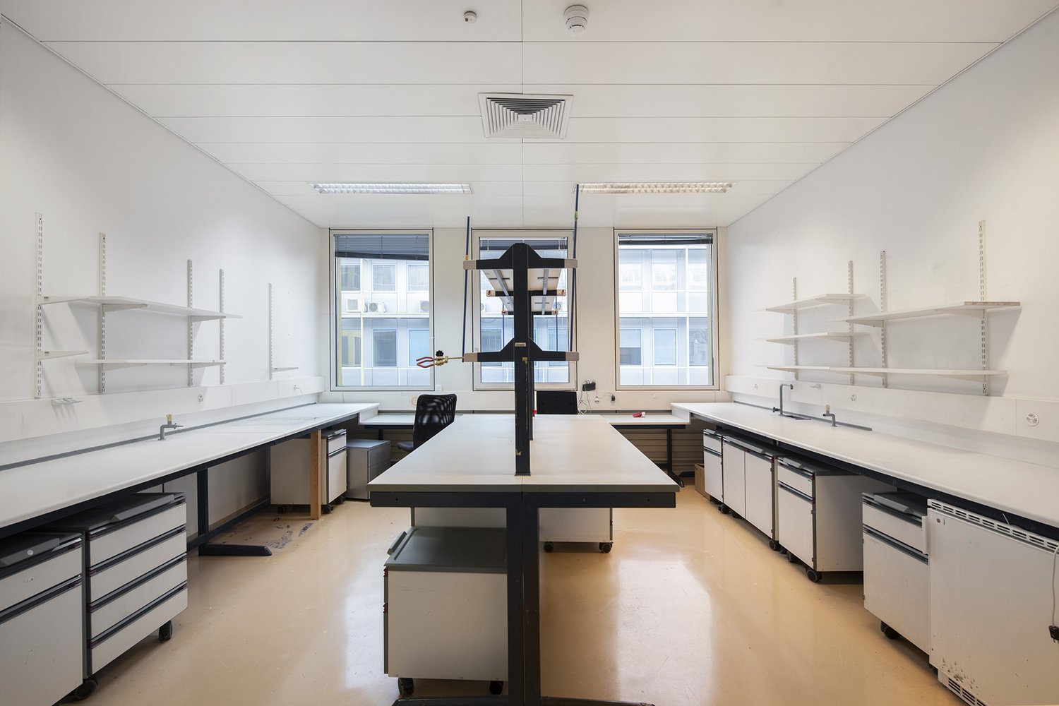 Laboratory with large white counter tops, metal carts, white walls, white shelves, windows with blinds