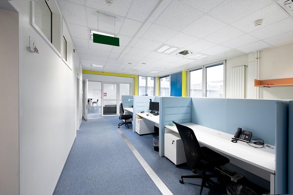 office cubicles with white desks, computer monitors, telephones, and black office chairs