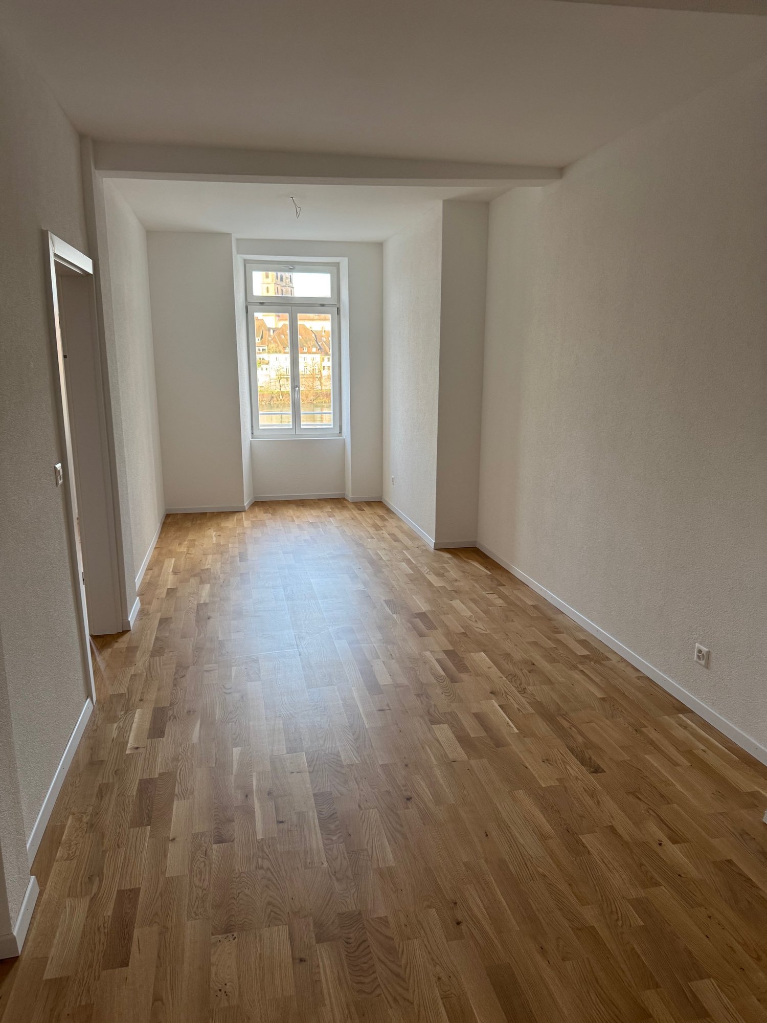 Empty room, wooden floor, white walls, window, power outlet