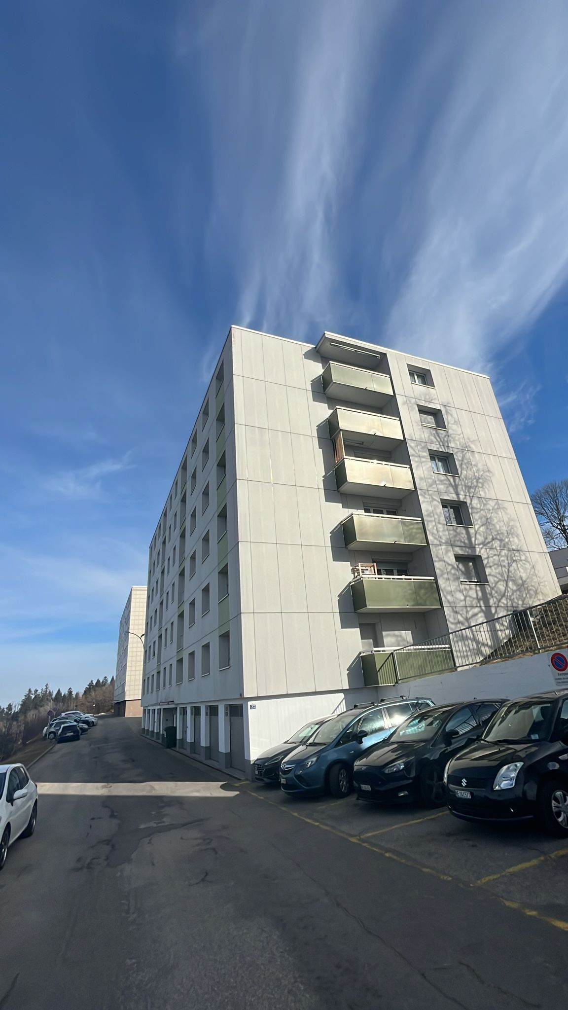 residential building, white exterior, multiple floors, balconies, ground floor parking lot