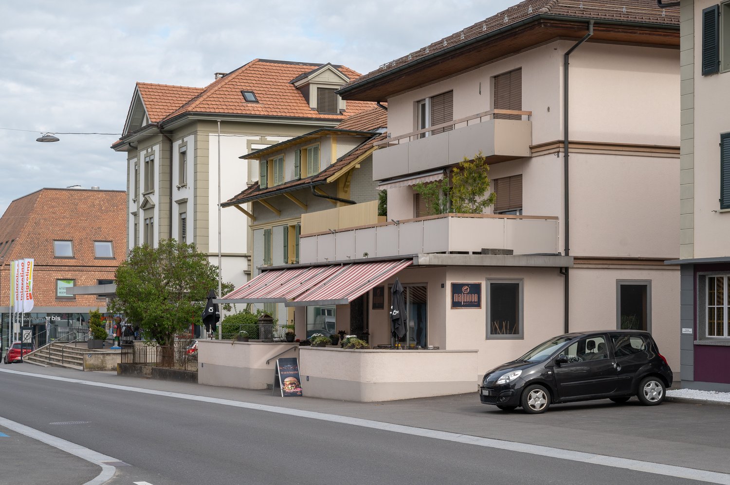 Building with a red awning, balcony, and a car parked in front