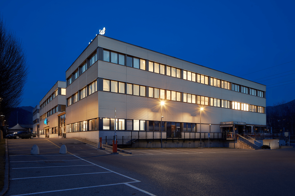 4 story building, multiple windows, entrance on the right side, parking lot in front, lit up with blue light