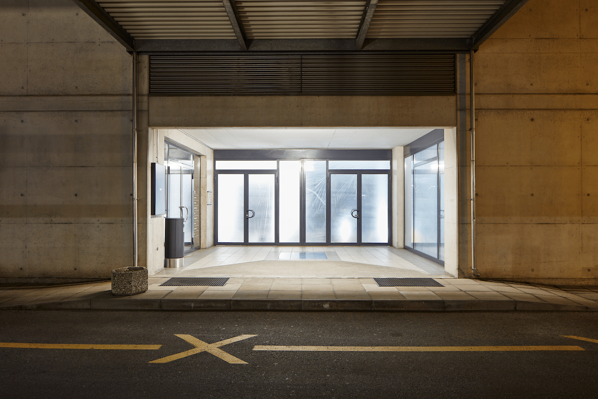 Empty entrance with double doors, tiled floor, large windows, concrete walls, small stone planter