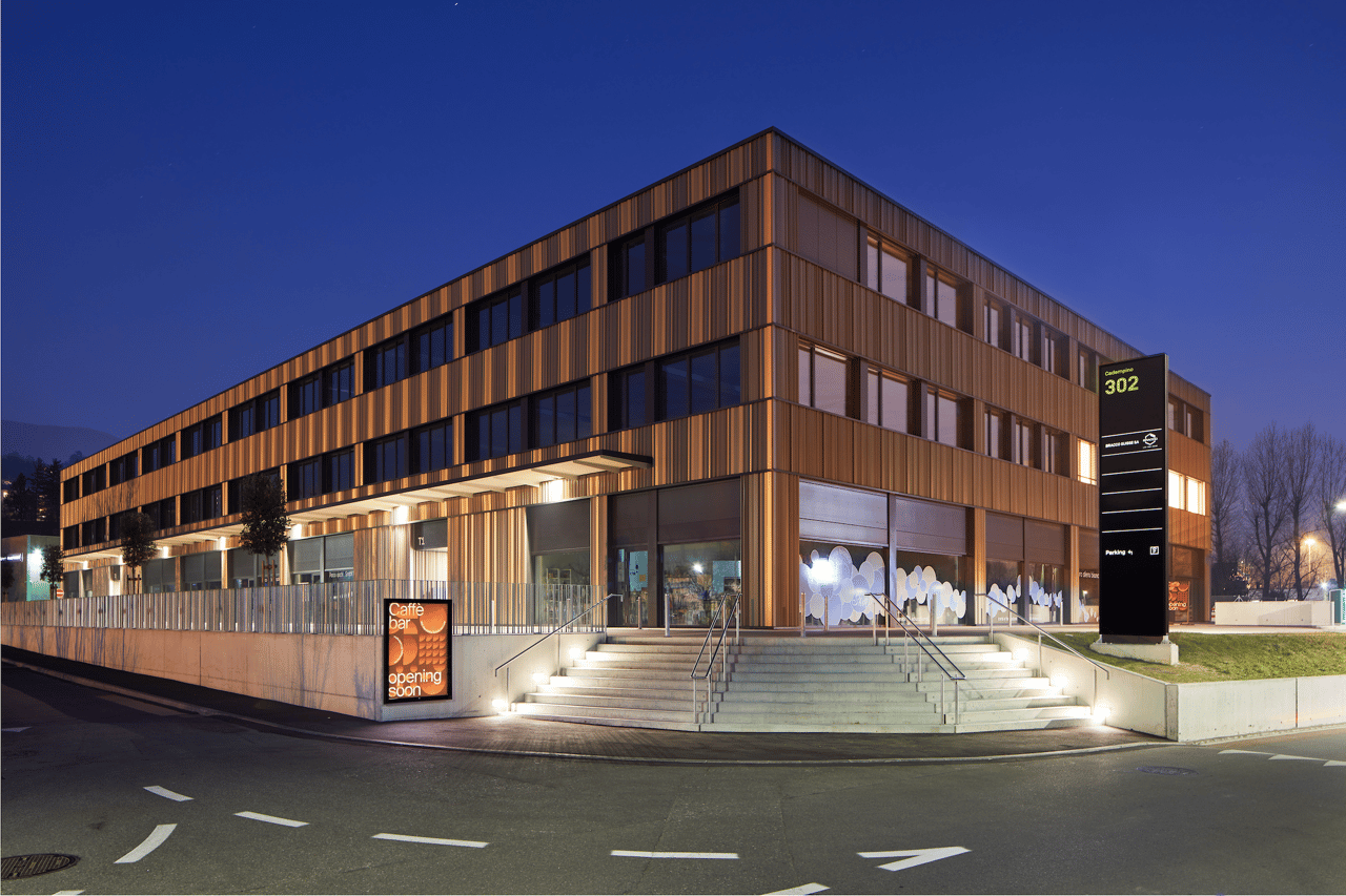modern multi-story building, brown exterior, glass windows, ground-level storefront, stairs, parking sign