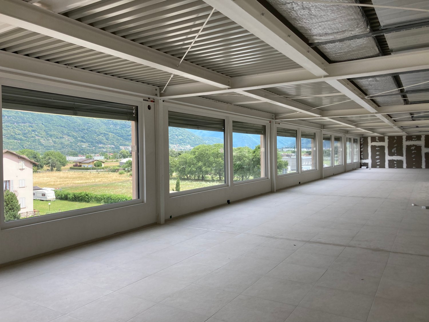 Empty room with large windows, tiled floor, metal ceiling, view of a field and mountains