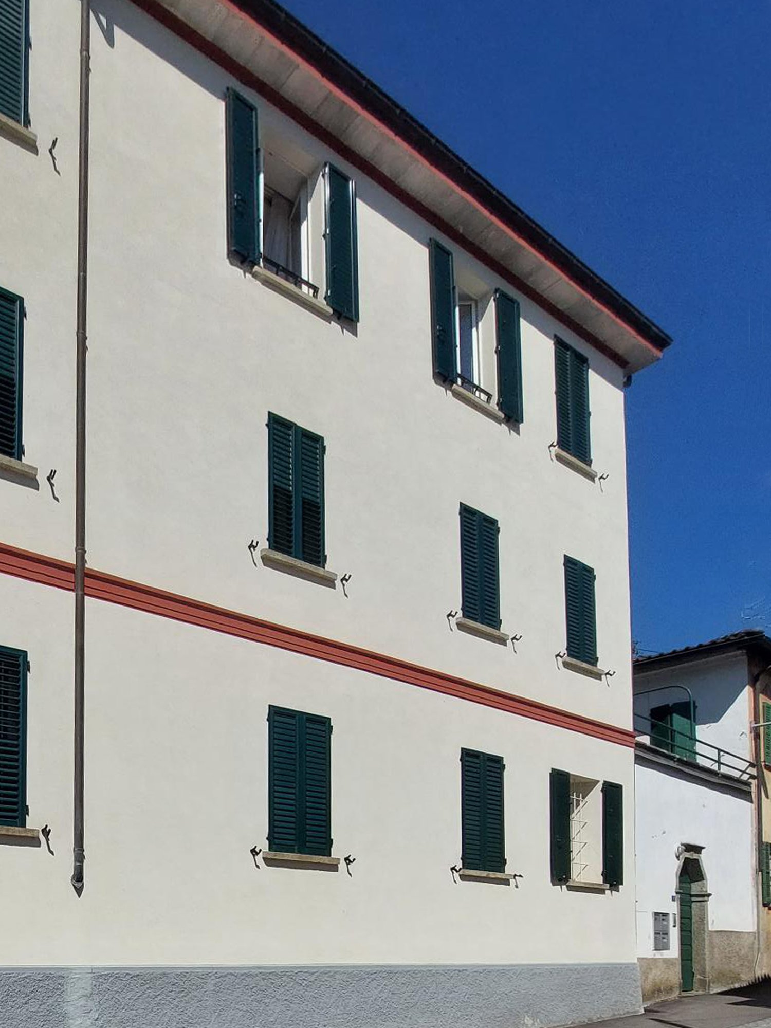A multi-story building with a cream-colored exterior, green shutters on the windows, and a red trim along the roofline.
