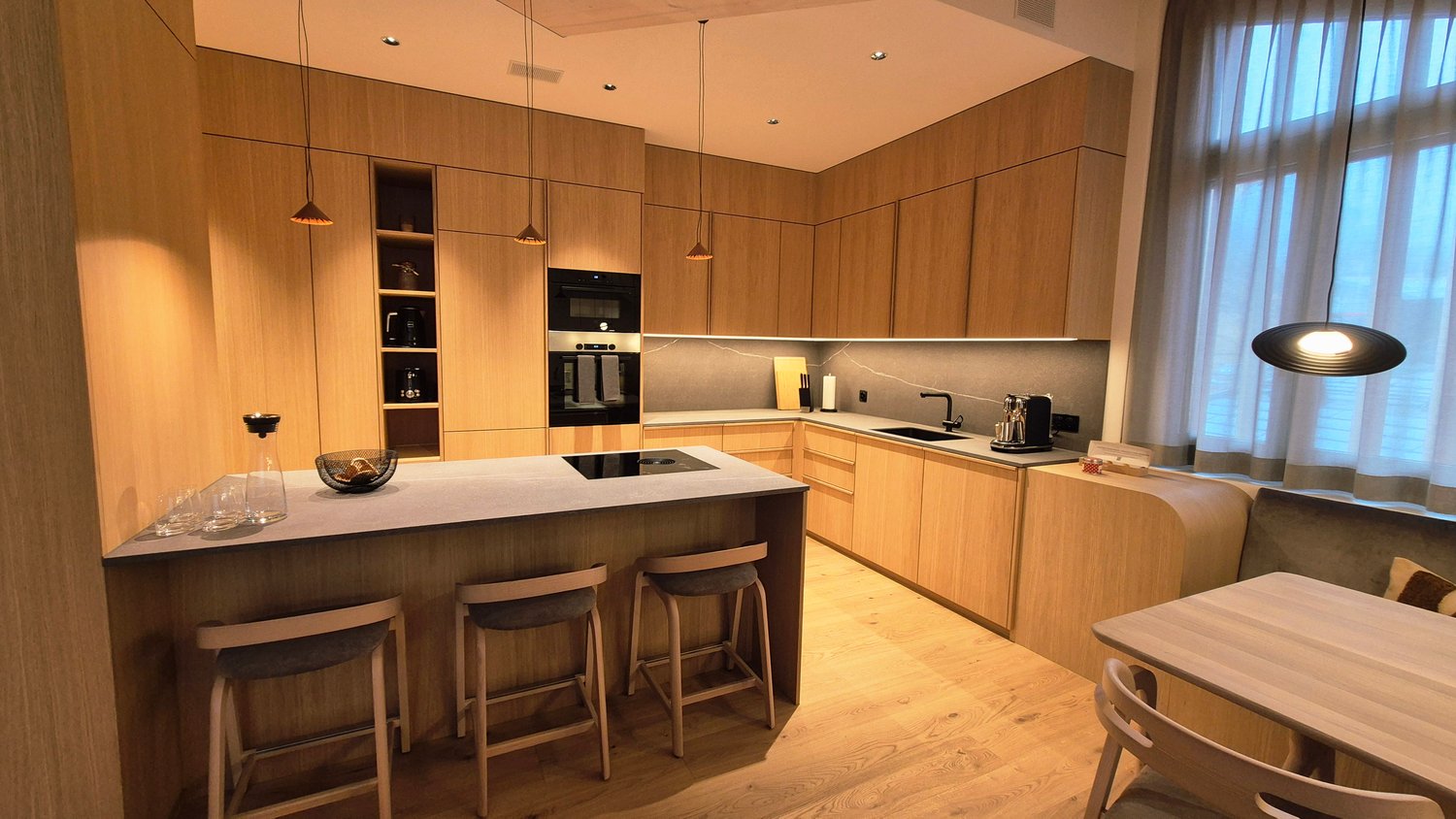 Open plan kitchen with island, white granite countertops, wooden cabinetry, modern appliances, seating area, ample windows