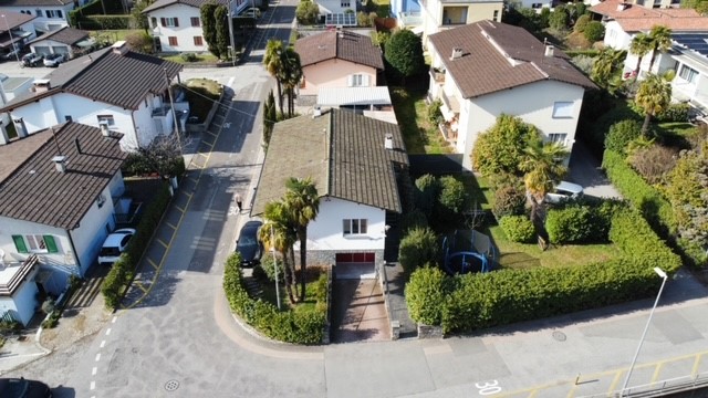 2 story house with red tile roof, surrounded by landscaped gardens and trees, with a garage and parking space visible.