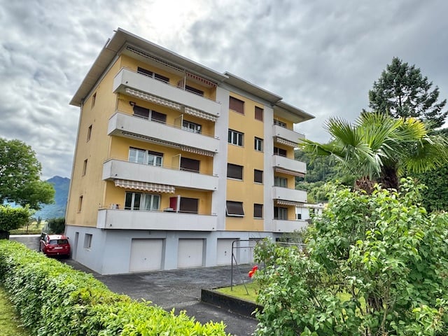 4-story apartment building with yellow exterior, balconies, and a parking area in the front
