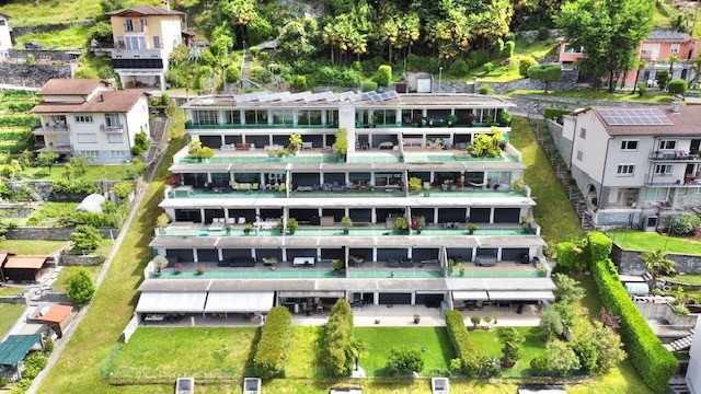 Multi-story apartment building with balconies, surrounded by lush greenery and trees