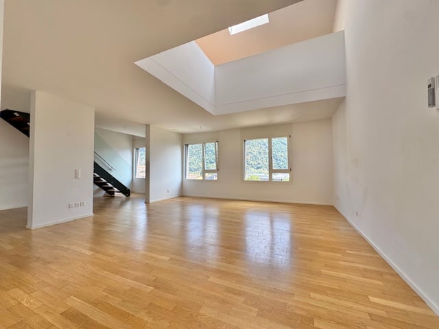 Spacious living room with hardwood floors, white walls, and a skylight providing natural light. The room has a clean, open layout.