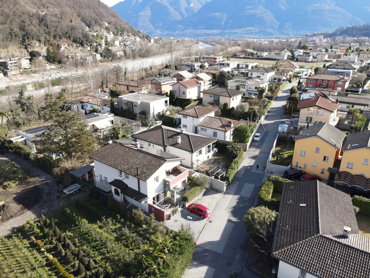 Aerial view of multiple houses with red cars parked outside, tiled roofs, driveways, and small gardens with trees