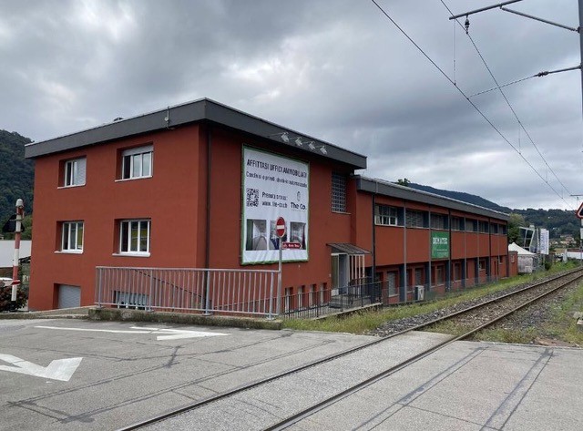 A multi-story red brick building with a flat roof, located next to a train track. The building appears to be a commercial or industrial facility.