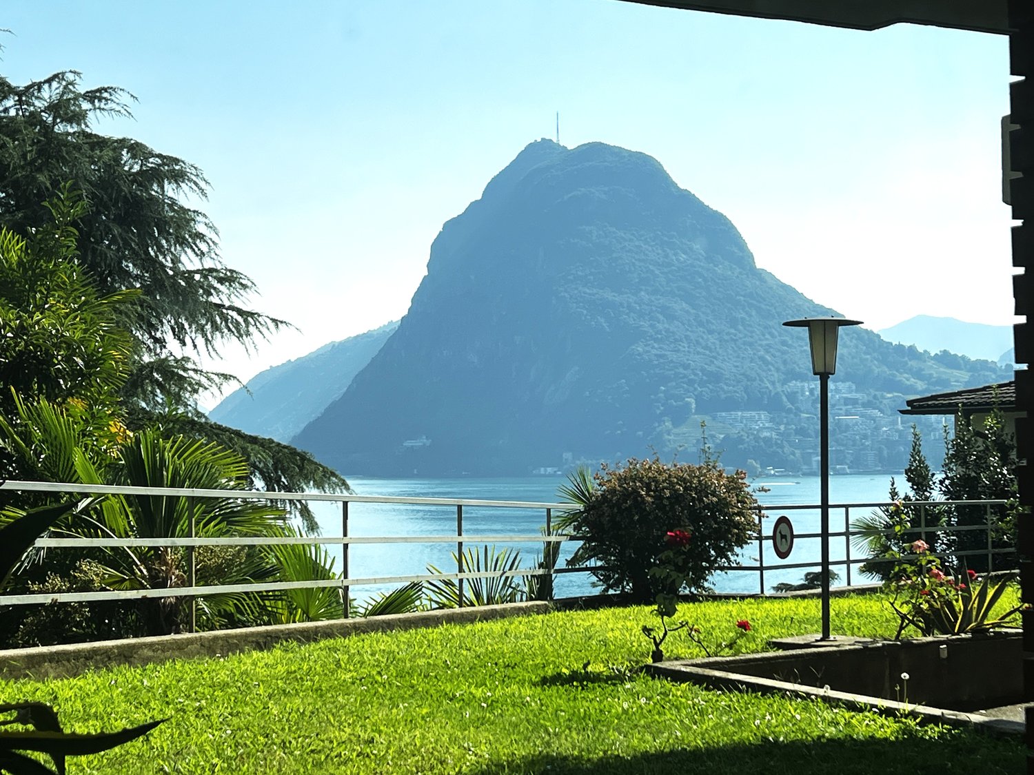 overlooking a mountain and lake, with a metal railing, street lamp, and lush greenery