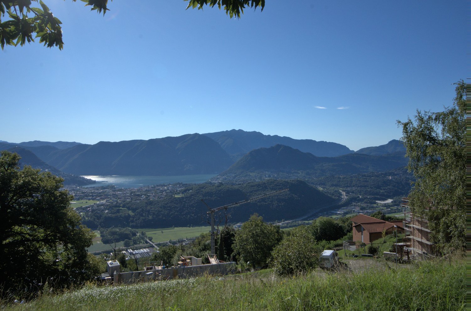 hillside with grass, trees, mountains, lake, town, construction site