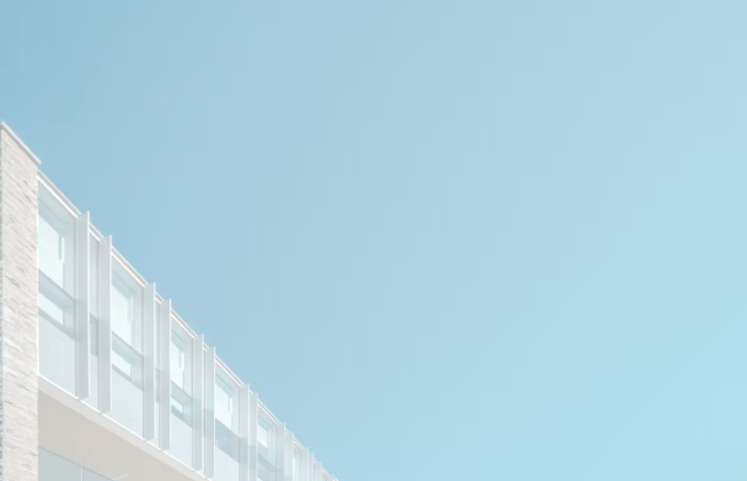 The image shows a modern, minimalist building with a series of large, rectangular windows arranged in a grid-like pattern. The building has a clean, white exterior and is set against a clear blue sky, creating a simple and elegant visual composition.