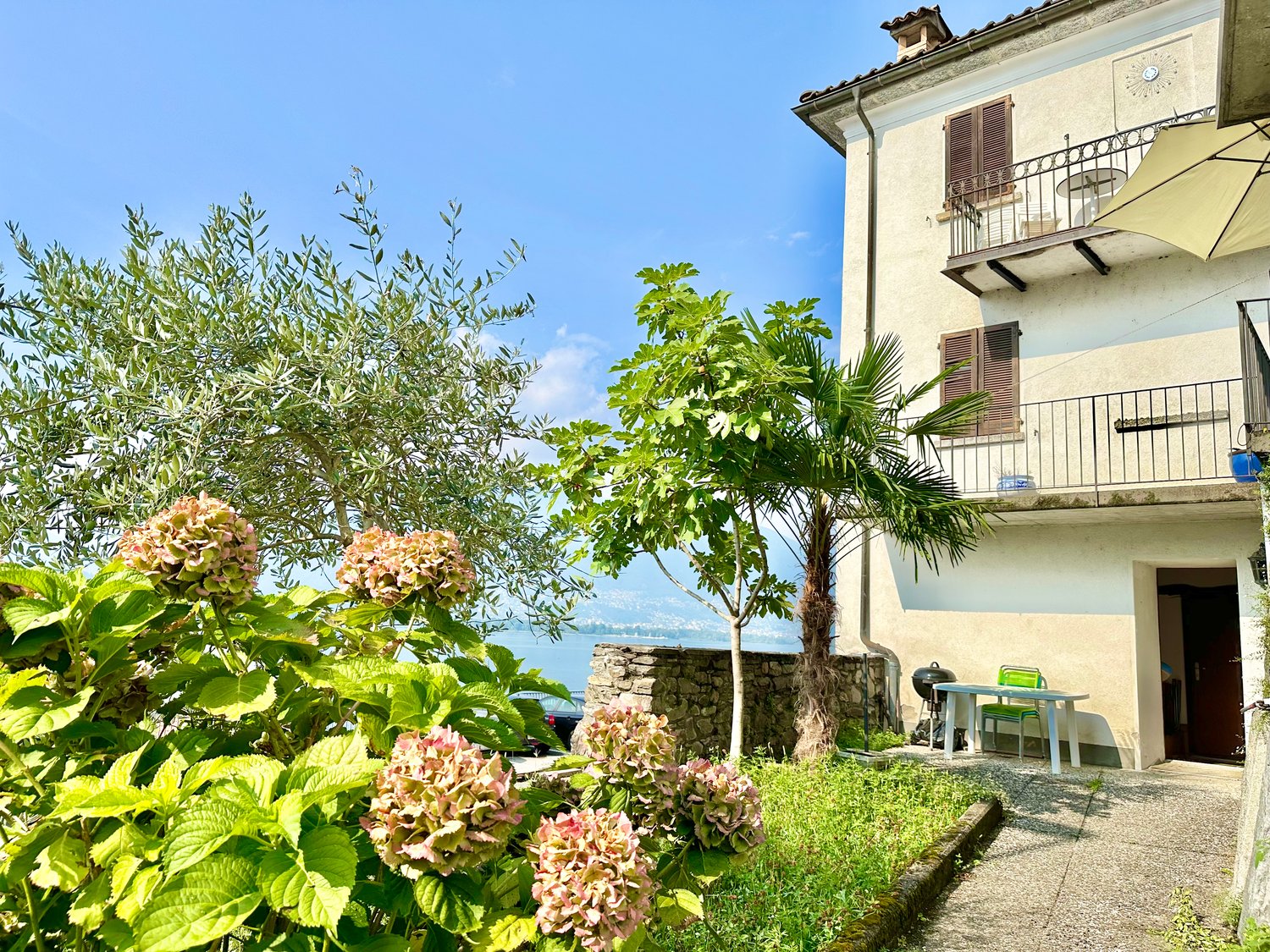 Two-story house with balcony, stone wall, garden, and lake view