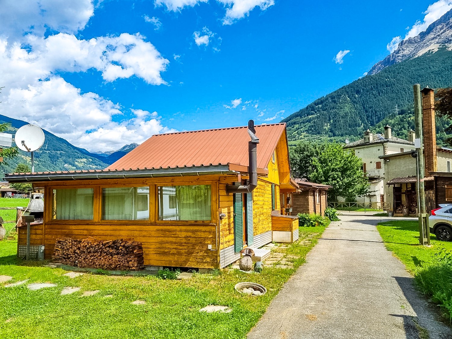wooden house, metal roof, window shutters, green lawn, mountains in background