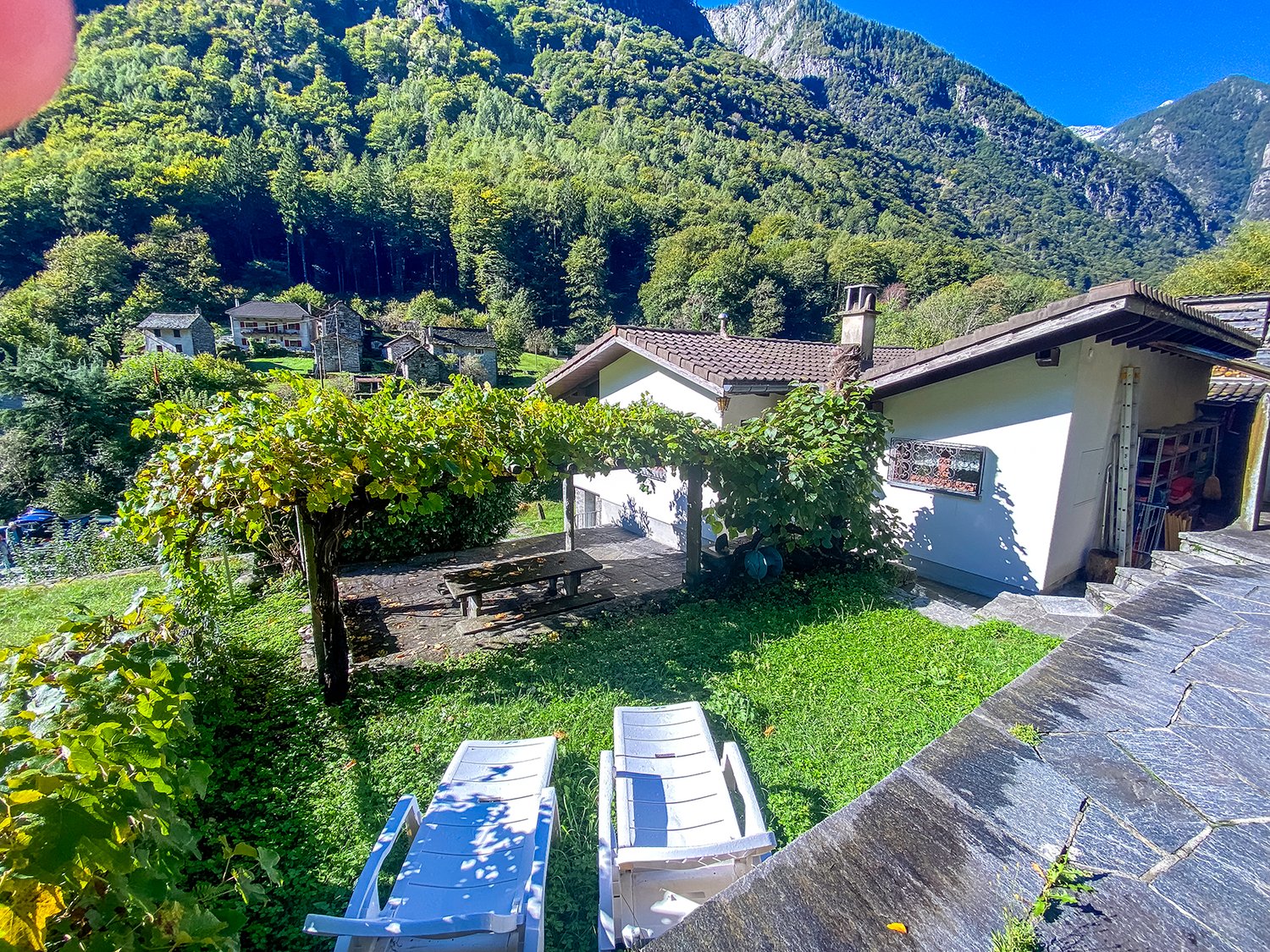 Mountain house, white walls, brown roof, large window, outdoor seating, green lawn, mountain view