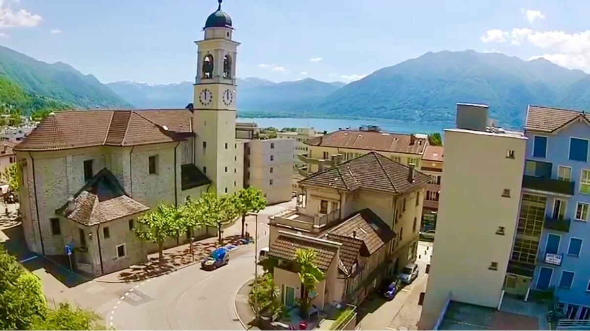 Church with a bell tower, several houses, road, lake, mountains in the background