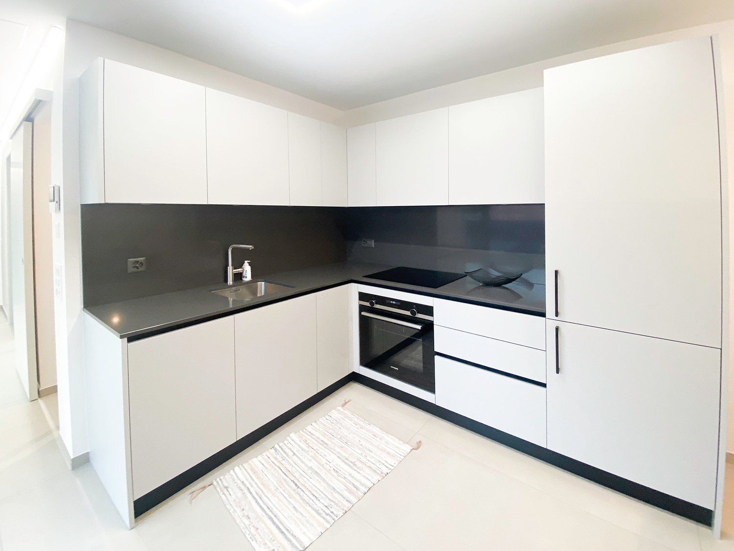 modern kitchen, white cabinets, black countertops, stainless steel sink, silver faucet, black oven, white tile flooring