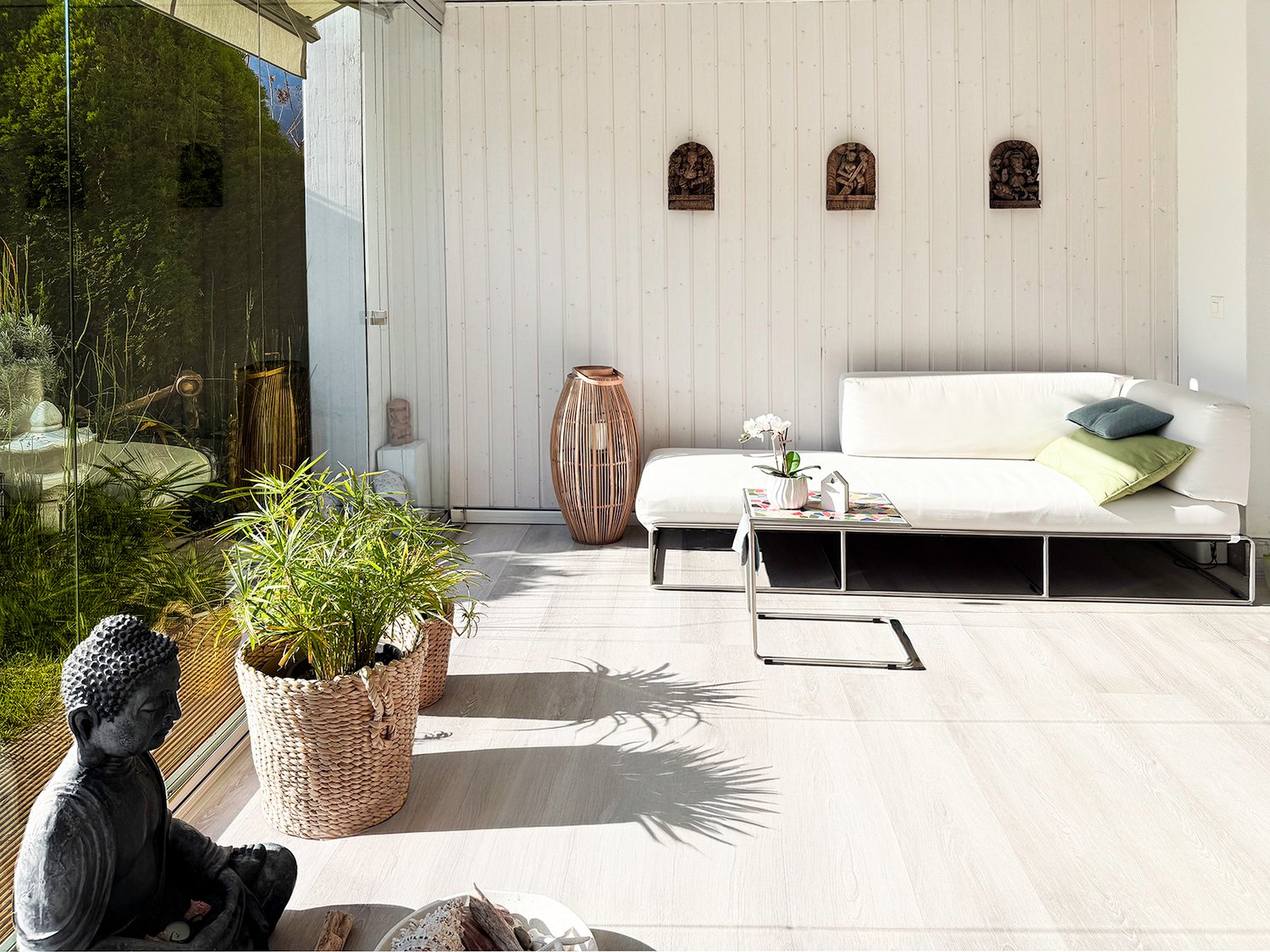 furnished terrace with white modern furniture, Buddha statue, glass wall, basket vase, and plants