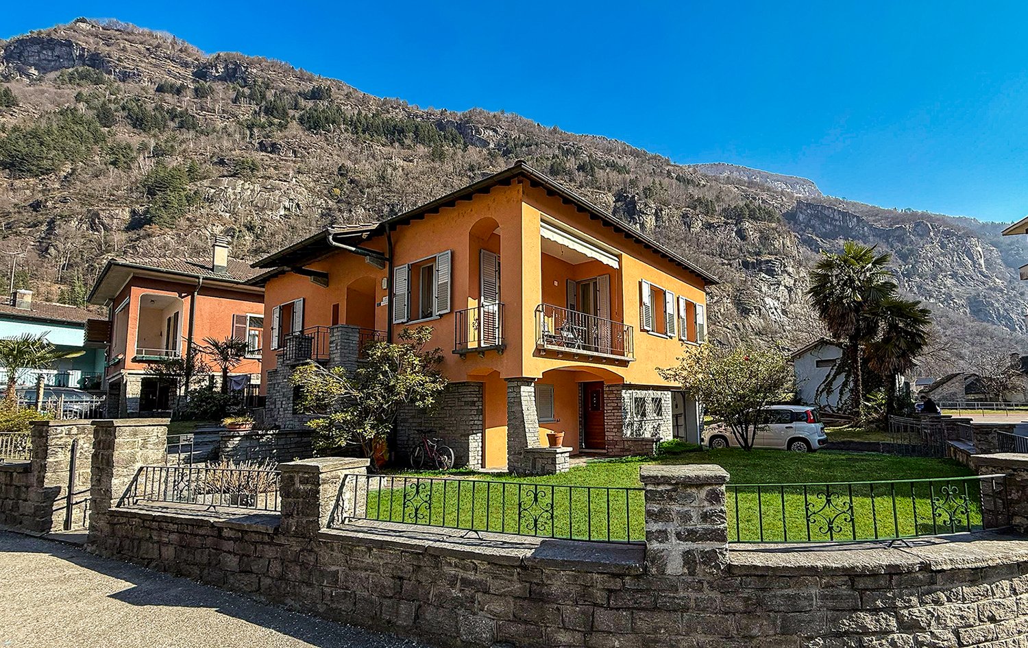 2-story house, orange exterior, brick wall foundation, multiple windows, fenced lawn, car parked, balcony on the first floor