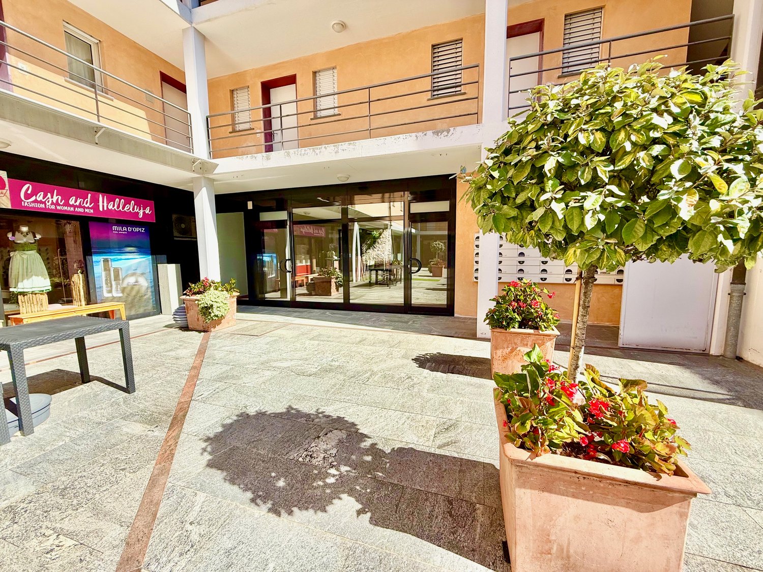 Apartment building entrance, balcony with railing, glass doors, greenery with flowering plants