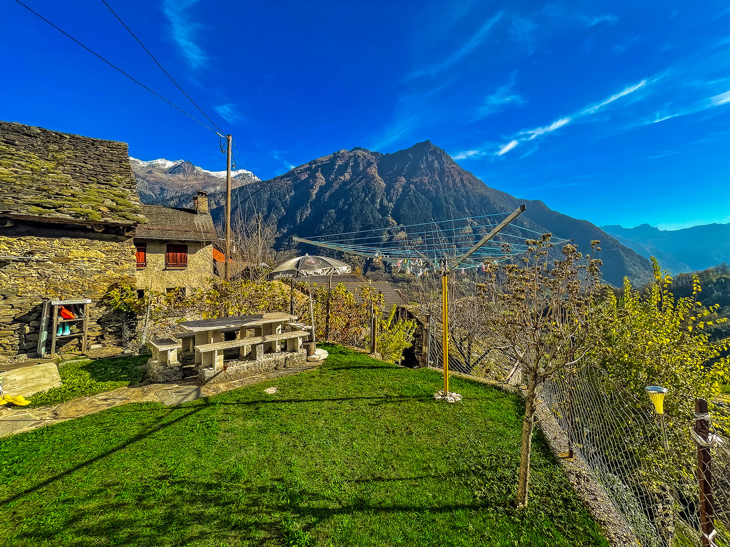 Stone house, stone bench, clothesline, green grass, mountain view