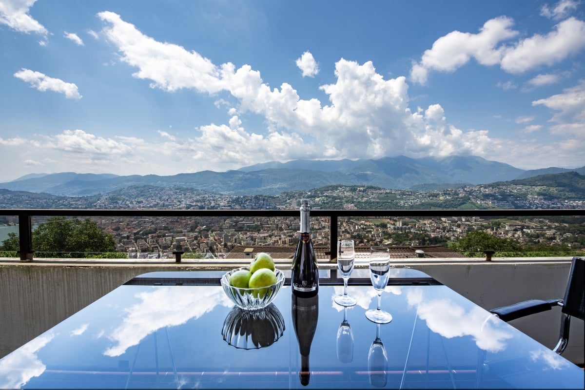 Table with view of mountains and city, bottle of champagne and two wine glasses