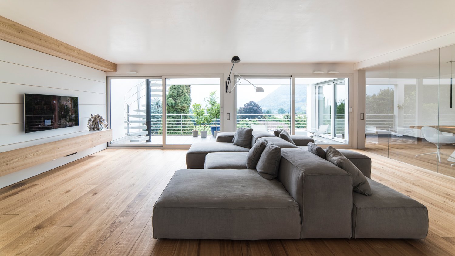 Wooden floor, large grey couch, TV, sliding glass doors to balcony