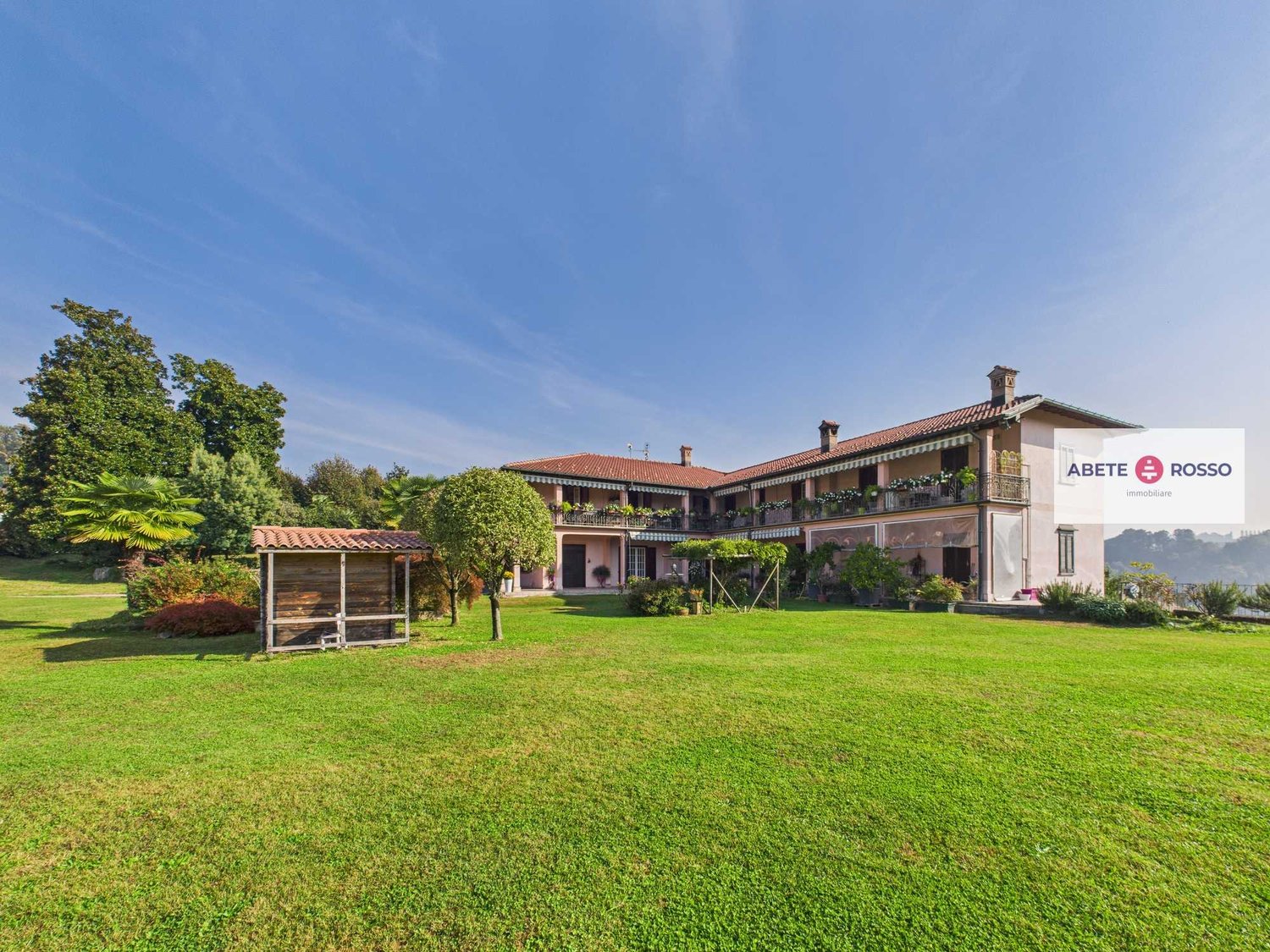 Two-story house, red roof, glass windows, surrounded by green lawn, balcony, trees